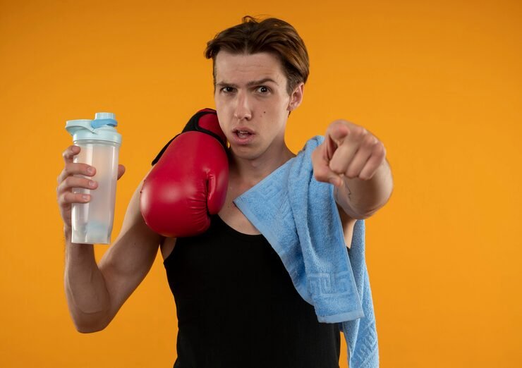 confident young sporty guy with towel boxing gloves shoulder holding water bottle showing you gesture isolated orange wall 141793 87606